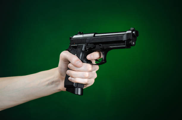 istock Firearms and murderer topic: human hand holding a gun on a dark green background isolated in studio 1045328664