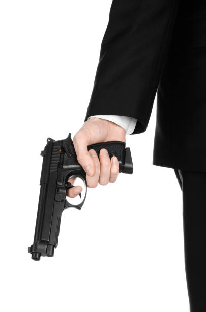 armes à feu et la sécurité thème : un homme dans un costume noir, tenant un pistolet sur un fond blanc isolé en studio - gun men spy suit photos et images de collection