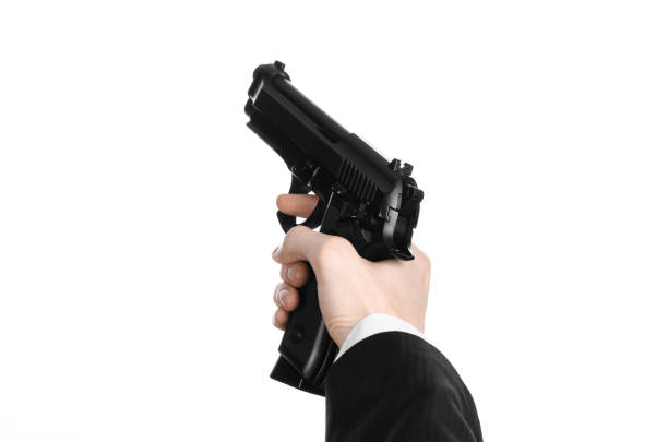 istock Firearms and security topic: a man in a black suit holding a gun on an isolated white background in studio 1045332384
