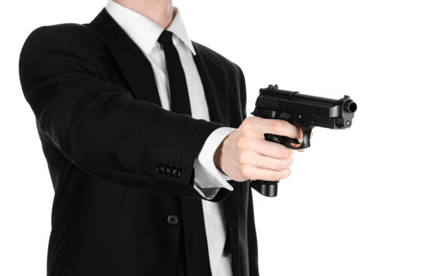 armes à feu et la sécurité thème : un homme dans un costume noir, tenant un pistolet sur un fond blanc isolé en studio - gun men spy suit photos et images de collection
