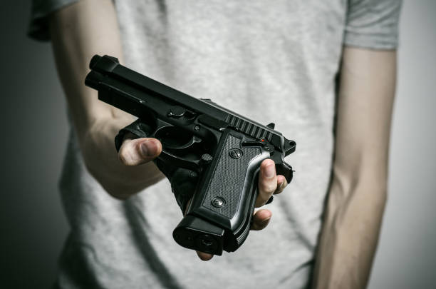 istock Horror and firearms topic: suicide with a gun on a gray background in the studio 1045336220