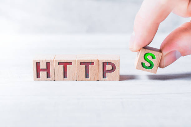 The Word HTTPS Formed By Wooden Blocks And Arranged By Male Fingers On A White Table stock photo