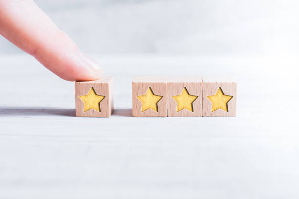 4 Star Rating Formed By Wooden Blocks And Arranged By A Male Finger On A White Table stock photo