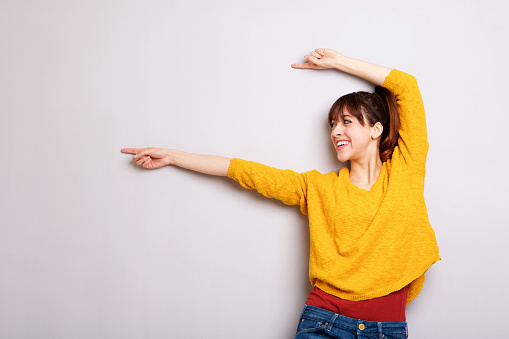 Portrait of cheerful young woman pointing finger against gray background
