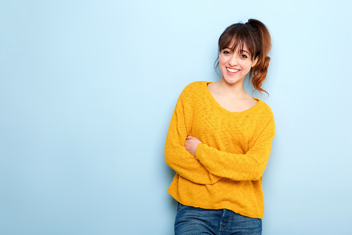 Portrait of smiling young woman with arms crossed against blue background