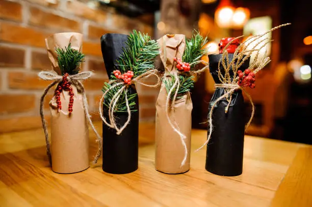 Four adorable christmas decorated bottles with ribbons and fir-tree branch on the wooden table on the background of brick wall