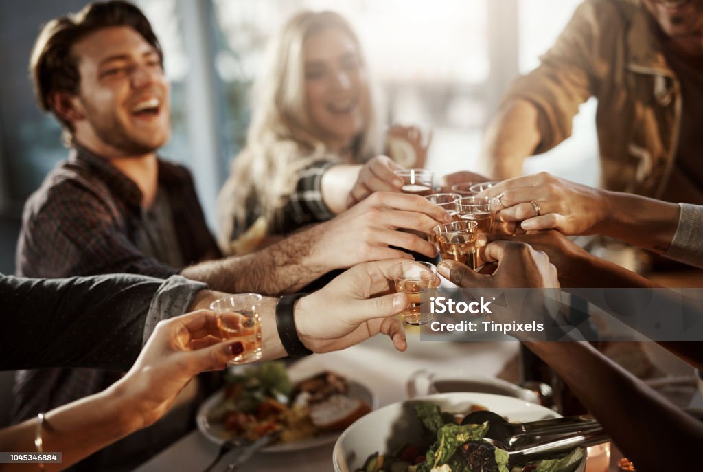 Friends know how to have fun Shot of a group of young friends making a toast at a dinner party Shot Glass Stock Photo