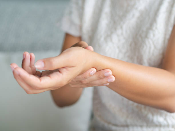 la giovane donna in primo piano seduta sul divano tiene il polso. lesioni alla mano, sensazione di dolore. assistenza sanitaria e concetto medico. - wrist foto e immagini stock