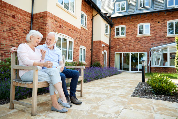 Retired Couple Sitting On Bench With Hot Drink In Assisted Living Facility Retired Couple Sitting On Bench With Hot Drink In Assisted Living Facility retirement community stock pictures, royalty-free photos & images