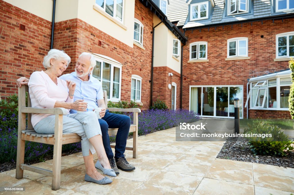 Casal de aposentados sentado no banco com bebida quente no asilo - Foto de stock de Terceira idade royalty-free