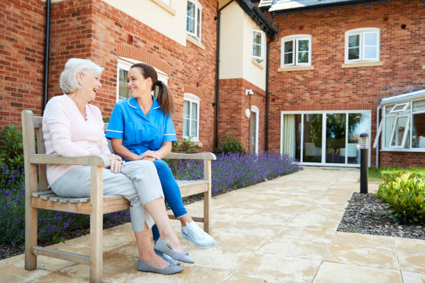 Senior Woman Sitting On Bench And Talking With Nurse In Retirement Home Senior Woman Sitting On Bench And Talking With Nurse In Retirement Home retirement community stock pictures, royalty-free photos & images