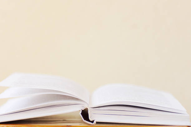 istock Opened book lying on wooden table blank white wall background. College school university education learning literacy concept. Poster banner with copy space 1045360240