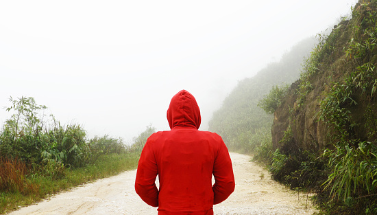 Man in red hoodie standing in front of misty mountain path