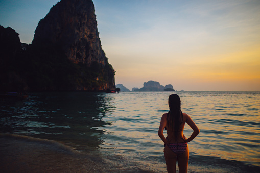 VIntage toned image of a young woman after a night swim, enjoying the beautiful view on the monumental cliffs at the popular Railay beach in Krabi province in Thailand.