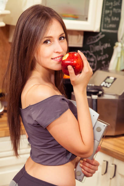 giovane bella sportiva che mangia mela mentre tiene la bilancia di peso. - spartan apple foto e immagini stock