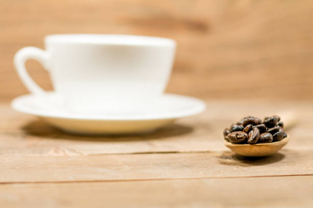 Coffee beans in a spoon and coffee cup on wood background