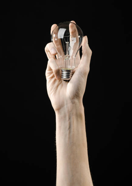 istock Energy consumption and energy saving topic: human hand holding a light bulb on black background in studio 1045383404