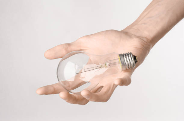 istock Energy consumption and energy saving topic: human hand holding a light bulb on a white background in studio 1045384250