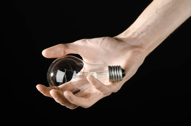 istock Energy consumption and energy saving topic: human hand holding a light bulb on black background in studio 1045386692