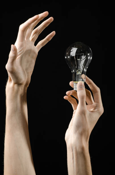 istock Energy consumption and energy saving topic: human hand holding a light bulb on black background in studio 1045387274