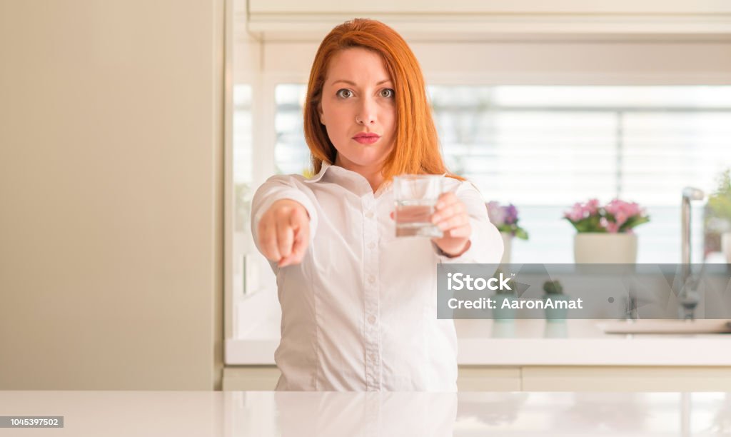 Thirsty redhead woman and glass of water pointing with finger to the camera and to you, hand sign, positive and confident gesture from the front Adult Stock Photo