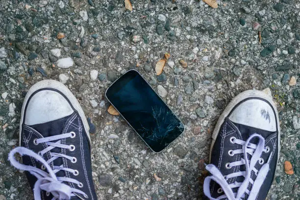 Standing over a broken smartphone on the street.