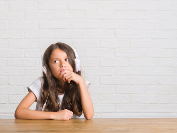 istock Young hispanic kid sitting on the table wearing headphones serious face thinking about question, very confused idea 1045408964