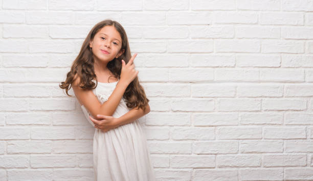 istock Young hispanic kid over white brick wall with a big smile on face, pointing with hand and finger to the side looking at the camera. 1045413876