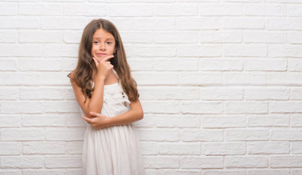 istock Young hispanic kid over white brick wall looking confident at the camera with smile with crossed arms and hand raised on chin. Thinking positive. 1045414146