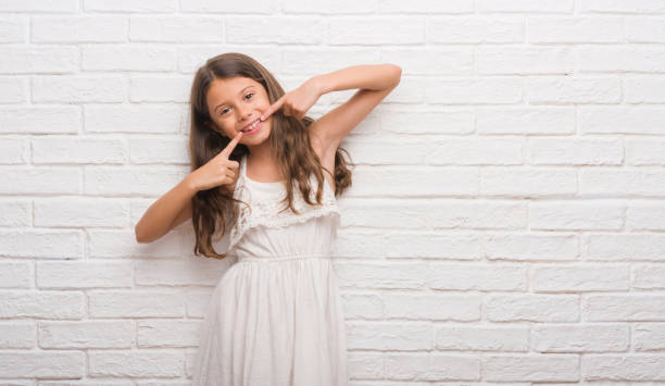istock Young hispanic kid over white brick wall smiling confident showing and pointing with fingers teeth and mouth. Health concept. 1045414226