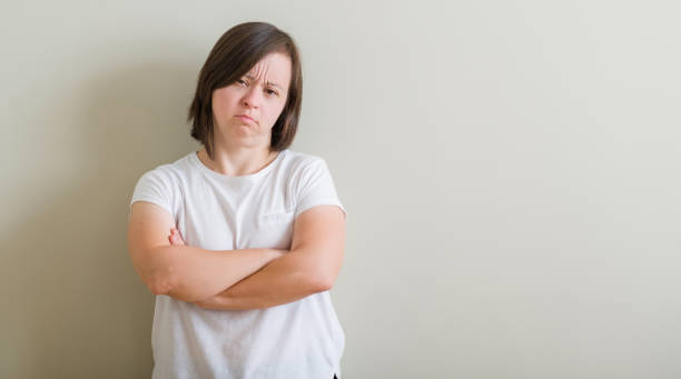 istock Down syndrome woman standing over wall skeptic and nervous, disapproving expression on face with crossed arms. Negative person. 1045415008