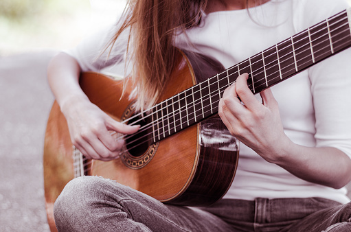Close-up of a guitar fretboard played by a blonde long haired girl outdoors.