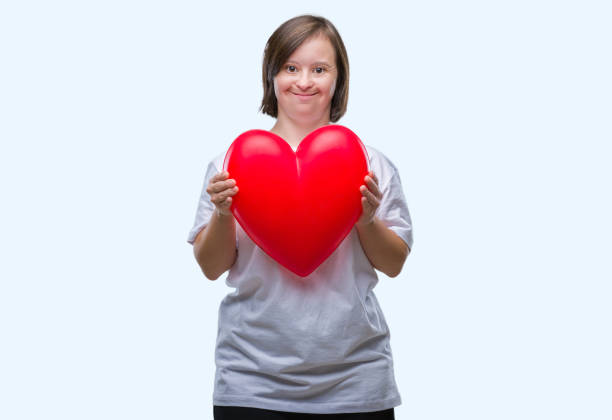 junge frau mit down-syndrom hält rotes herz über isolierte hintergrund mit ein glückliches gesicht stehen und lächeln mit einem zuversichtlich lächeln zeigt zähne - toothy smile relaxation white healthcare and medicine stock-fotos und bilder