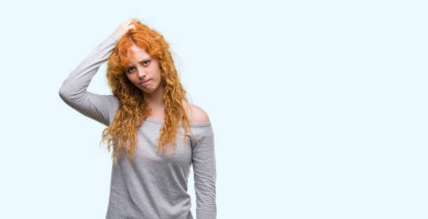 istock Young redhead woman confuse and wonder about question. Uncertain with doubt, thinking with hand on head. Pensive concept. 1045421256