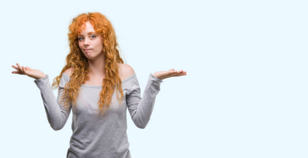 istock Young redhead woman clueless and confused expression with arms and hands raised. Doubt concept. 1045421498