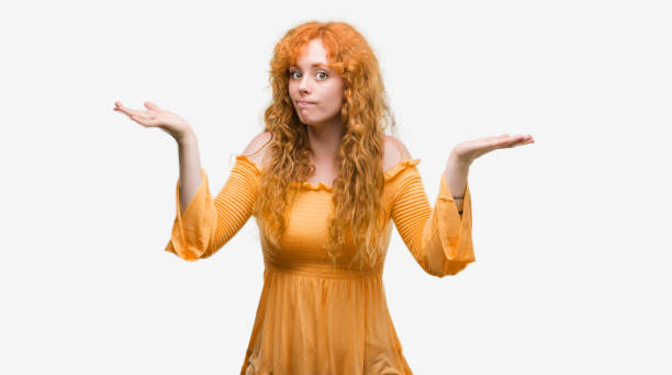 istock Young redhead woman clueless and confused expression with arms and hands raised. Doubt concept. 1045425404