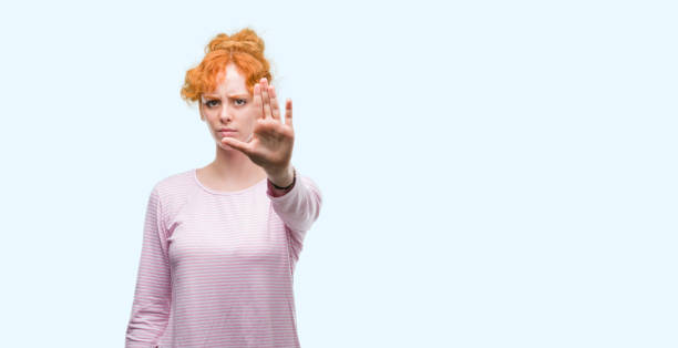 istock Young redhead woman doing stop sing with palm of the hand. Warning expression with negative and serious gesture on the face. 1045427616