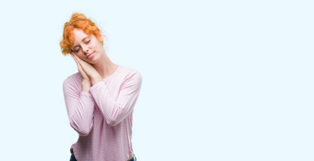 istock Young redhead woman sleeping tired dreaming and posing with hands together while smiling with closed eyes. 1045428348