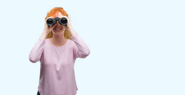 istock Young redhead woman looking through binoculars with a happy face standing and smiling with a confident smile showing teeth 1045428618
