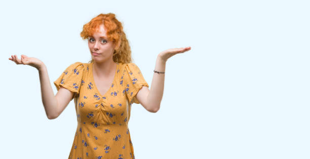 istock Young redhead woman clueless and confused expression with arms and hands raised. Doubt concept. 1045431462