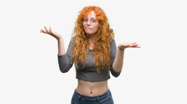 istock Young redhead woman clueless and confused expression with arms and hands raised. Doubt concept. 1045433528