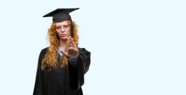 istock Young redhead student woman wearing graduated uniform with open hand doing stop sign with serious and confident expression, defense gesture 1045434374