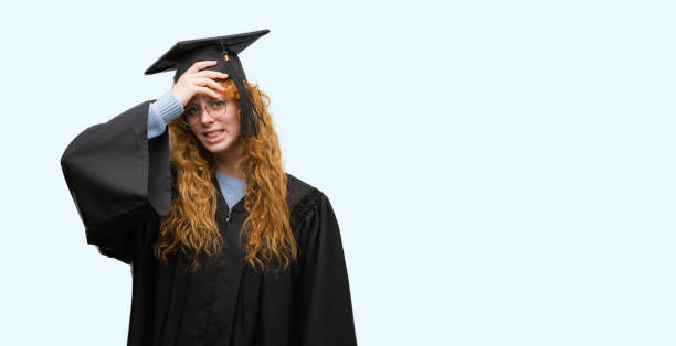 istock Young redhead student woman wearing graduated uniform stressed with hand on head, shocked with shame and surprise face, angry and frustrated. Fear and upset for mistake. 1045434428