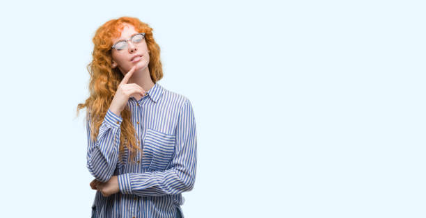istock Young redhead bussines woman with hand on chin thinking about question, pensive expression. Smiling with thoughtful face. Doubt concept. 1045435824