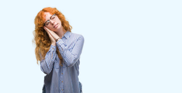 istock Young redhead bussines woman sleeping tired dreaming and posing with hands together while smiling with closed eyes. 1045438092