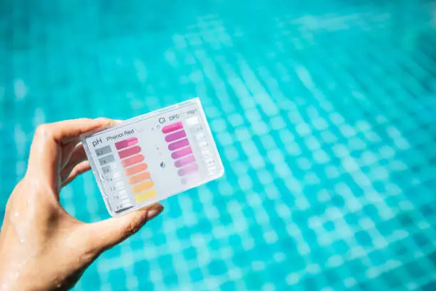Photo of Swimming pool water testing test kit in girl hand over blurred blue swimming pool water background
