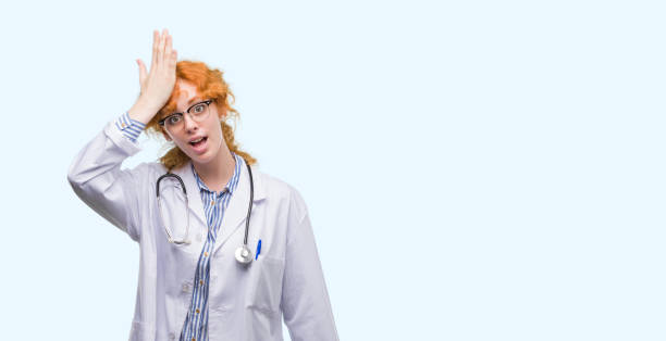 istock Young redhead woman wearing doctor uniform surprised with hand on head for mistake, remember error. Forgot, bad memory concept. 1045438432