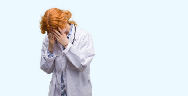 istock Young redhead woman wearing doctor uniform with sad expression covering face with hands while crying. Depression concept. 1045438490