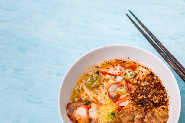 istock Closeup egg noodle soup with grill pork in white bowl on blue table background 1045439206