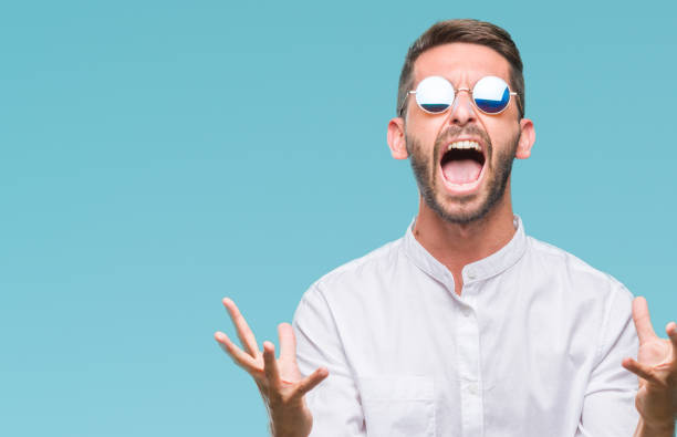 istock Young handsome man wearing glasses over isolated background crazy and mad shouting and yelling with aggressive expression and arms raised. Frustration concept. 1045447934